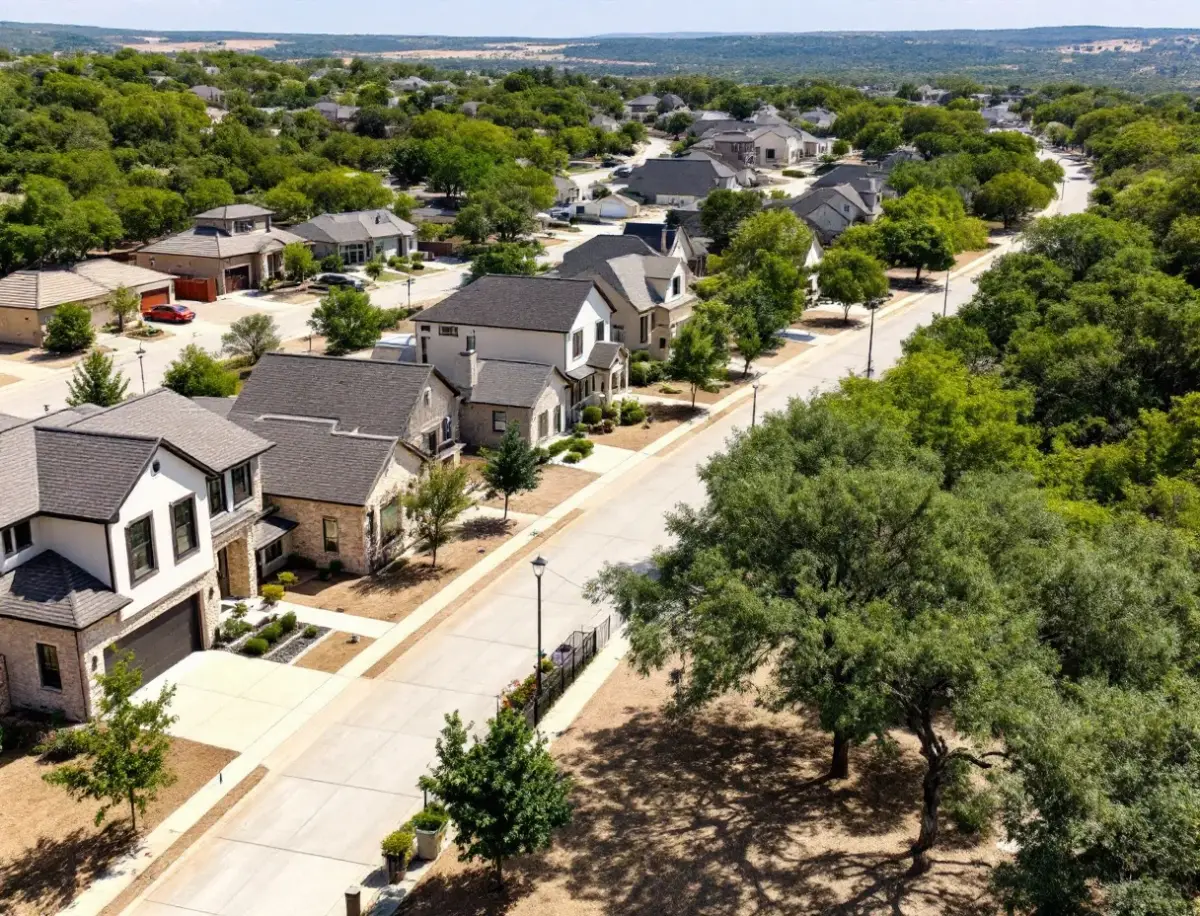 Two-story stone and hardie homes along a curving sidewalk street with maturing shade trees and a greenbelt behind