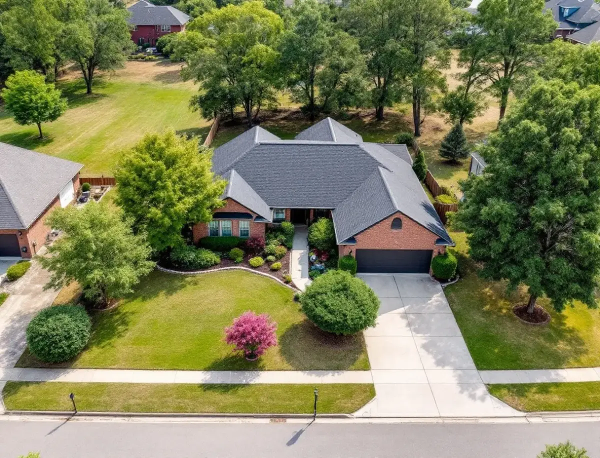 A single-story limestone ranch home shaded by mature live oaks on a deep quarter-acre lot, long driveway and split-rail fence out front